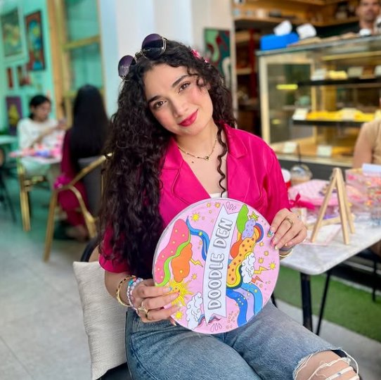 Shazmé Malik, founder of Doodle Den, holding a hand-painted Doodle Den sign